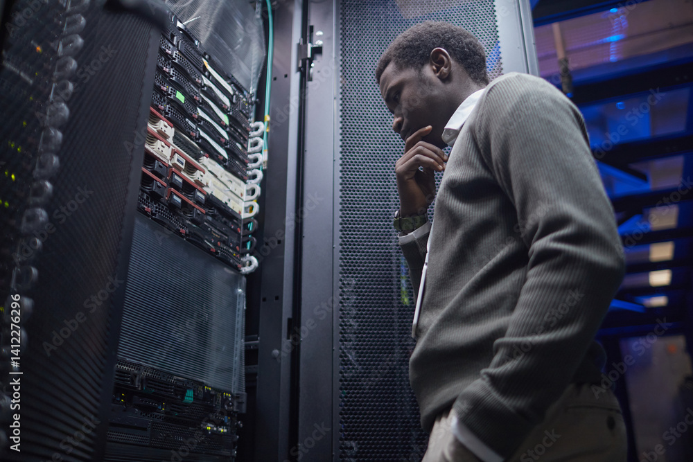 Poster black person contemplating server maintenance in data center with thoughtful expression examining ra