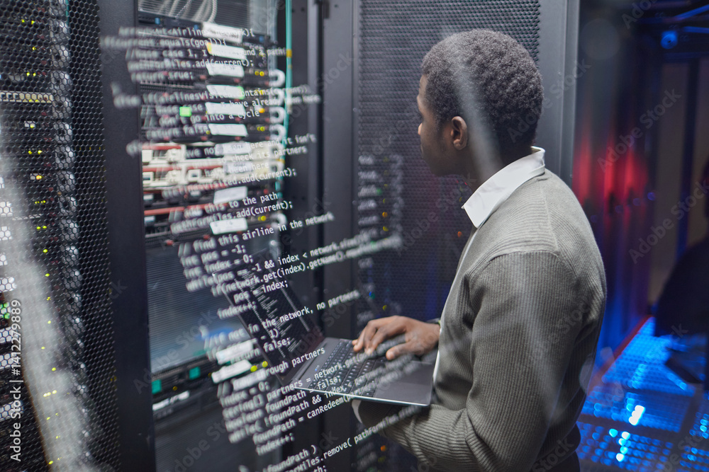Poster african american technician checking data systems in modern data center, monitoring status on laptop