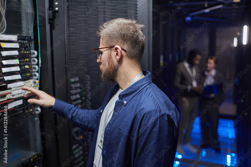 Poster technician in blue shirt configuring server rack in data center with colleagues in background. led l