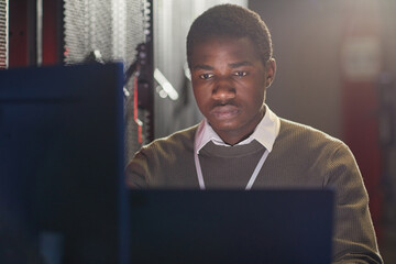 Young man focusing on work in modern tech environment, with computer screens and electronic...