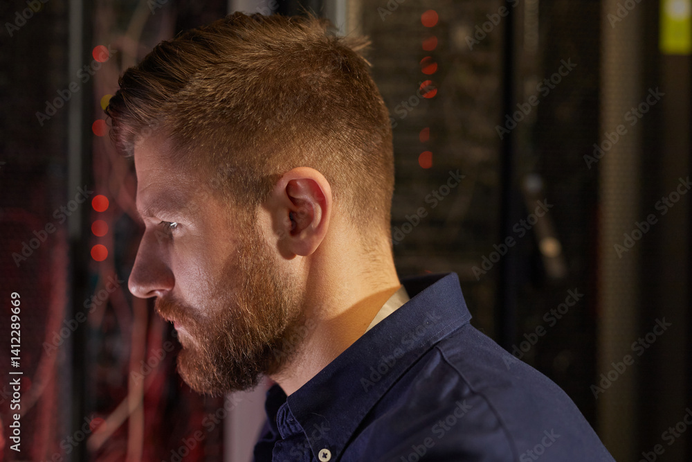 Aufkleber man with beard intently examining server racks in a data center wearing blue shirt, side profile vie