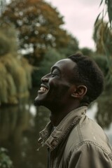 A smiling black man enjoys a moment of happiness with a scenic lake and trees in the background.