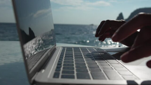 Laptop, Ocean, Work - Person using laptop on a boat with ocean in the background.