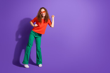 Young stylish woman in colorful outfit dancing on a purple background, expressing joy and charm in a casual fashion style
