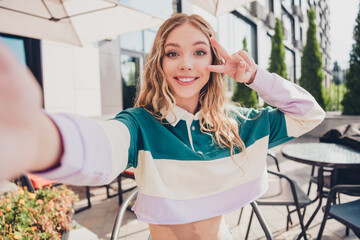 Photo of pretty young girl take selfie show v-sign eye wear top free time city center street cafe...