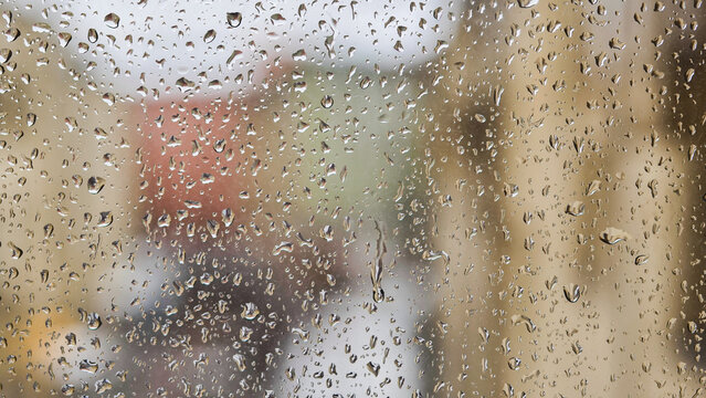 Raindrops flowing on window glass during rainy day blurring city buildings in background - Powered by Adobe