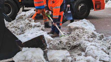 Municipal workers removing snow from road with shovels and truck