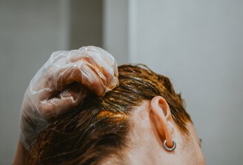 Naklejka premium A woman applies hair dye with a special brush wearing gloves at home in the bathroom