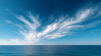 Obraz premium Delicate cirrus clouds stretch across clear blue sky over calm ocean, creating serene scene