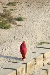 A woman wearing a red sari on the bank of the river