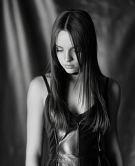 Naklejka premium A beautiful woman with an emotional expression is captured in a closeup portrait, looking down with her long hair set against a dark background in black and white