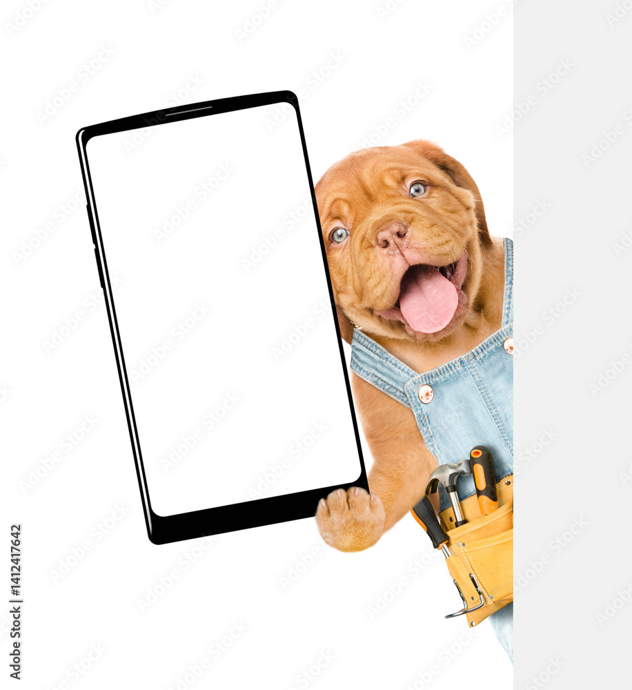 Leinwandbilder happy mastiff puppy wearing denim overalls with tool belt shows big smartphone with blank screen beh