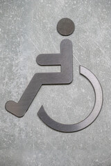Metal wheelchair accessibility symbol on textured concrete wall. Close-up sign icon. Disability and...