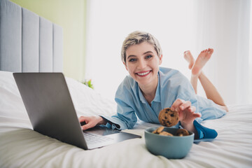 Smiling Woman Enjoying Chocolate Chip Cookies and Working on Laptop in Comfortable Bedroom Setting