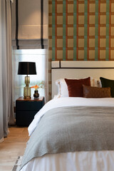 stylish bedroom interior design with wallpaper and black patterned pillows on bed and decorative table lamp.