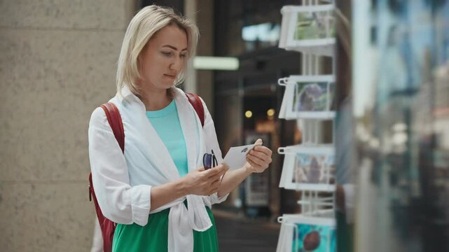 A female tourist browses Australian postcards at a charming outdoor kiosk. The display rack showcases local landmarks and wildlife, capturing the essence of travel memories under warm sunlight.