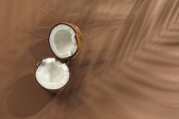 Fresh coconut and shadow cast by tropical palm on beige background, top view. Space for text