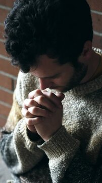 Vertical scene of a young bearded man sitting on the ground in prayer, silently asking for strength during a difficult personal moment