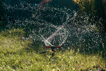 Garden sprinkler watering green grass with water drops in sunlight