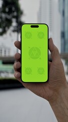 GREEN SCREEN CHROMA KEY Smartphone with a green screen held outdoors in a modern urban setting with high-rise buildings and traffic in the background
