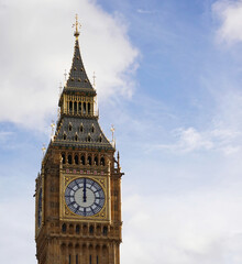 A closeup of Big Ben at 12 noon in Westminster, London against a cloudy blue sky. 