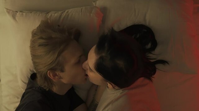 Top view young loving couple romantic time in bedroom. Man and woman half naked sensual lovers laying in bed together, passion, intimacy kissing, foreplay and bonding.