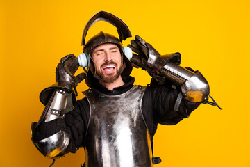Fototapeta premium Funny knight in full armor wearing headphones against a vibrant yellow background and enjoying modern music
