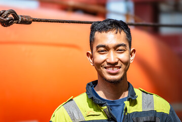 Portrait of a young Filipino marine engineer standing by the lifeboat on a merchant ship, beginning...