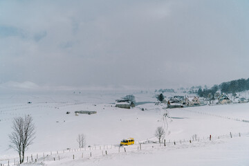 Yellow minibus drives along a snowy road in a small village