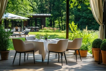 A white tablecloth table with four chairs set for dinner on a wooden patio with a lush green garden in the background