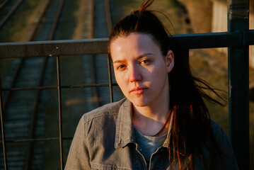 Thoughtful young woman on bridge at sunset with railway background
