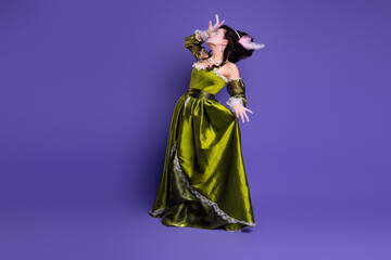Young woman in historical green dress posing theatrically over purple background, depicting themes...