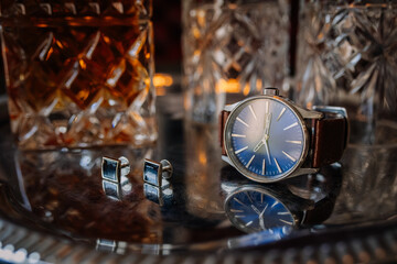 Close-up of a stylish wristwatch and cufflinks placed on a silver tray with crystal glasses and a...