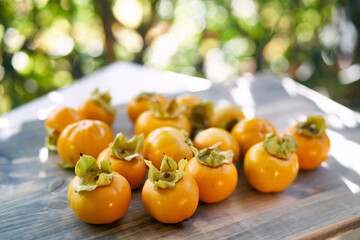 Juicy orange persimmons lie on a wooden table on the balcony in the sunlight