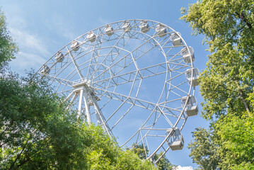 Ferris wheel in the city park in summer. A mechanical attraction in the form of a large vertically mounted wheel with passenger cabins attached to the rim. Entertainment for children and adults.