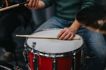 Close-up of a musician handling drumsticks over a red snare drum during a rehearsal.