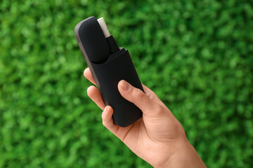 Female hand holding modern electronic cigar with stick against green nature background