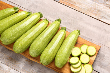 Board with many fresh green zucchini on grey wooden background