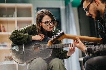 A young guitarist receives helpful guidance while rehearsing chords during a music session indoors.