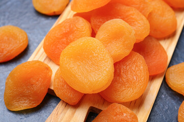 Wooden board with tasty dried apricots on blue background