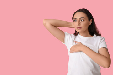 Young woman checking her breast on pink background. Cancer awareness concept