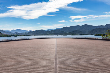 Empty wooden floor deck and beautiful blue lake with mountain range landscape under blue sky.