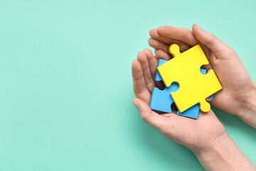 Female hands holding color puzzle on cyan background. Autistic disorder concept