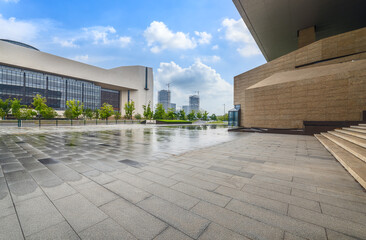 Obraz premium Wet empty stone floor pavement and modern office building exterior in city.