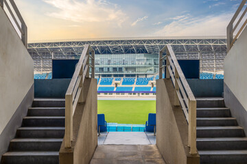 Entrance tunnel stairs leading to empty seats and green field in a modern sports stadium arena background. © zhao dongfang