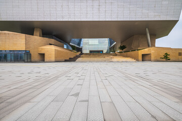 Empty stone floor plaza leading to a large modern architectural building exterior. © zhao dongfang