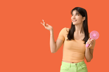 Young woman with mini fan showing something on orange background