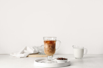 Glass cup of iced latte, bowl with coffee beans and jug of milk on white background