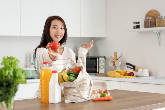 Young Asian woman unpacking fresh products from market in kitchen