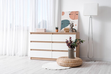 White chest of drawers with books, painting and eucalyptus branches near window